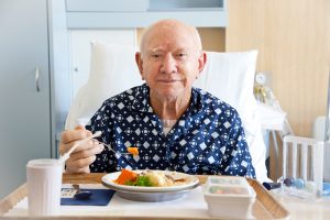 Senior male patient in hospital eating lunch